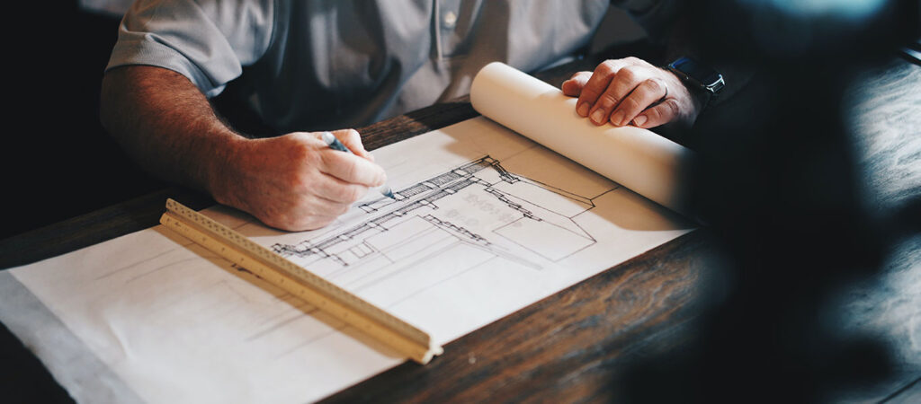An architect drawing building plans on drafting paper for his firms ideal project profile